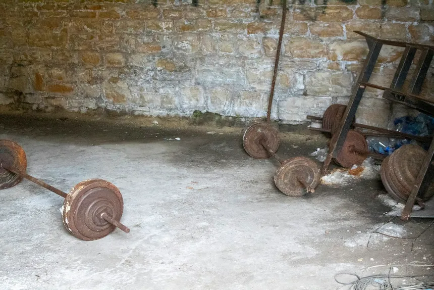 Rusted barbells and loose weight plates left on a bare concrete floor in a disused room