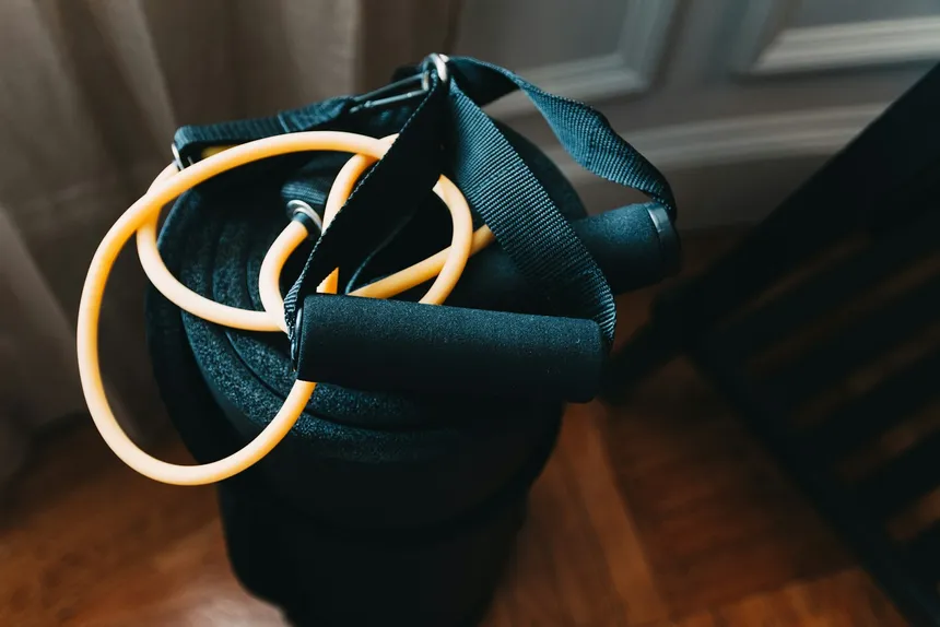 A resistance band with foam handles coiled on a dark surface in warm side light
