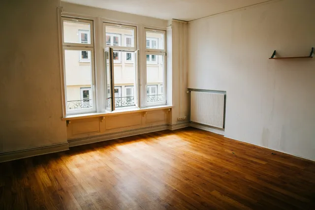 An empty room with a bare wooden floor and tall windows along one wall