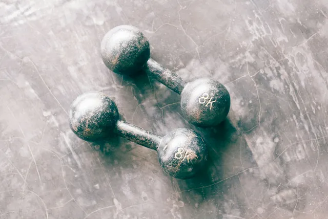 A pair of old dumbbells with the paint chipped away to bare metal, on a worn floor