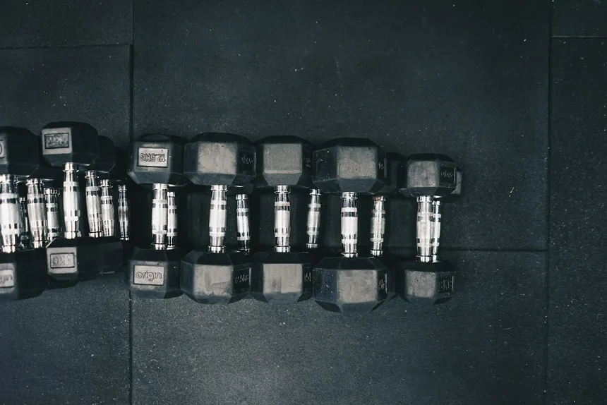 A long row of hex dumbbells laid out on a gym floor, from the lightest to the heaviest