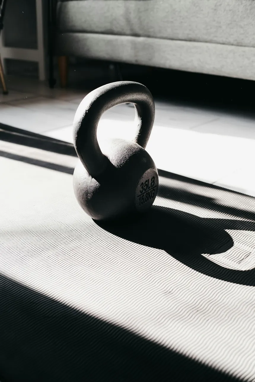 A single kettlebell throwing a long shadow across a mat in a sunlit room
