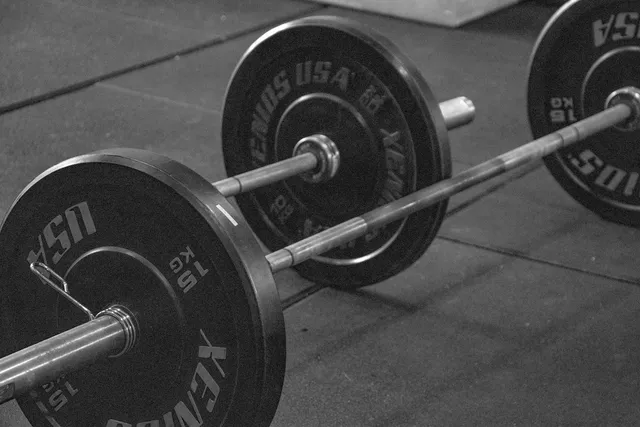 A loaded barbell resting on a gym floor, photographed in black and white from close to the ground