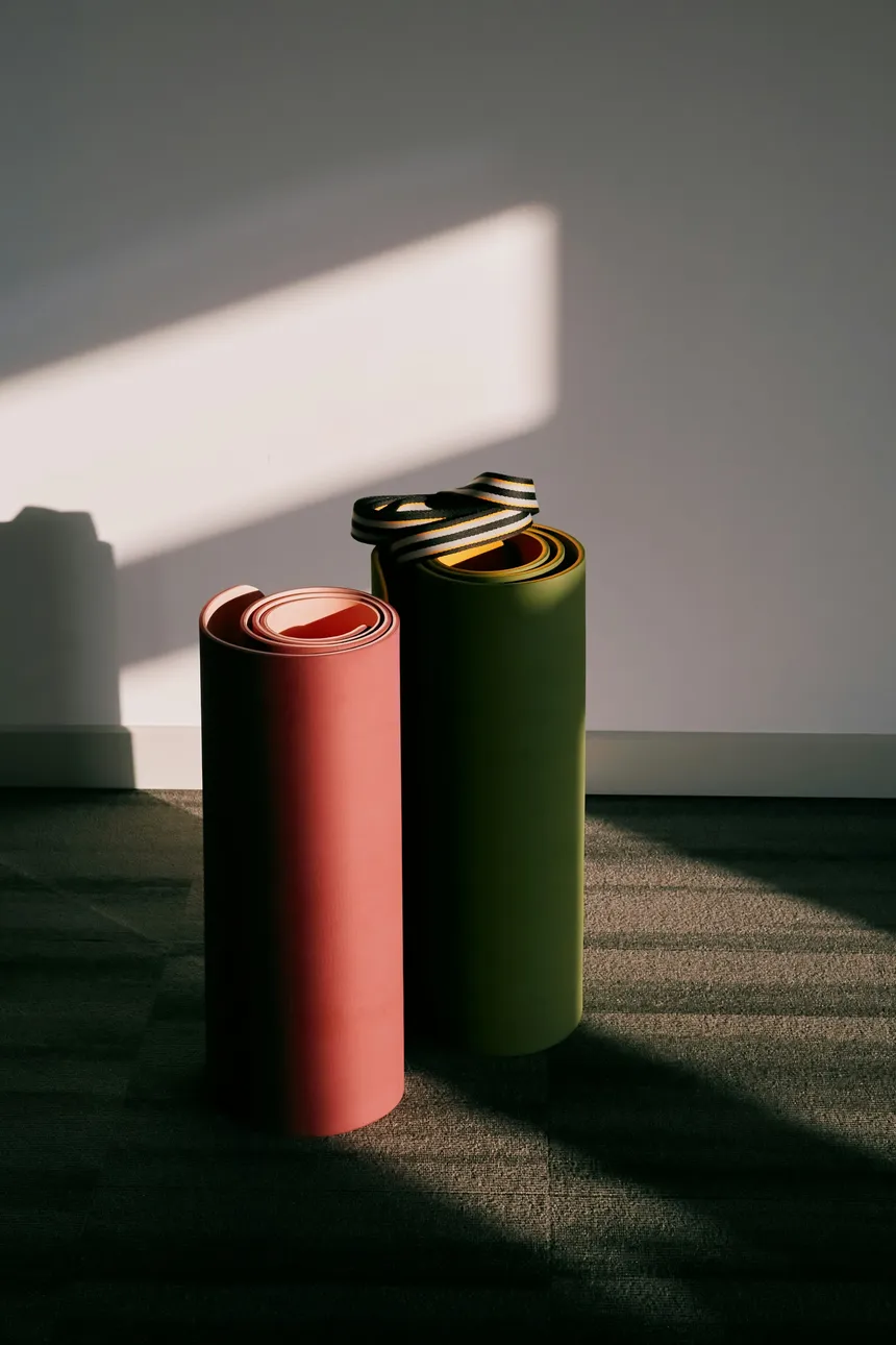 Two rolled exercise mats standing against a wall in a bare, sunlit corner