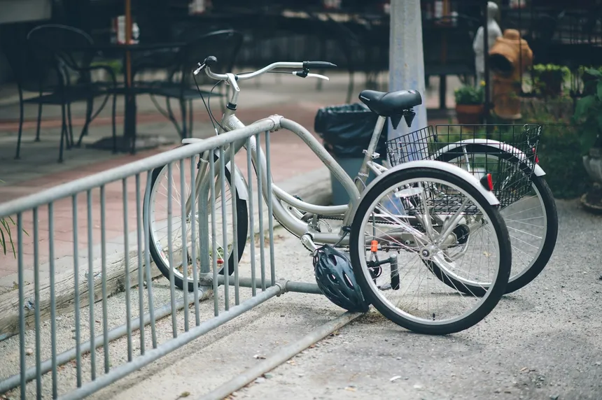 A three-wheeled trike parked at a railing, seen from behind so both rear wheels and the width between them are visible