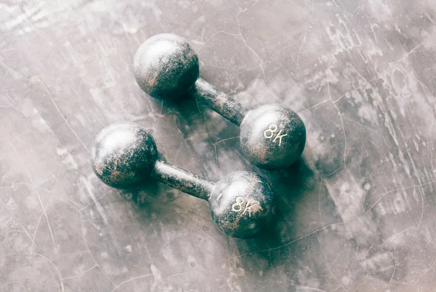 Two chrome dumbbells resting on a dark textured surface, lit from one side