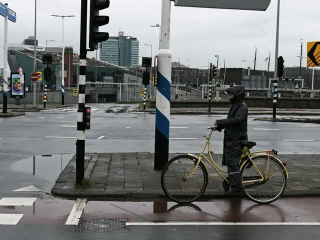 A rider waiting at a crossing on a wet street, the ordinary weather this question is actually about