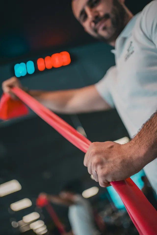 A man in a t-shirt drawing a red resistance band across his body, other bands stacked behind him
