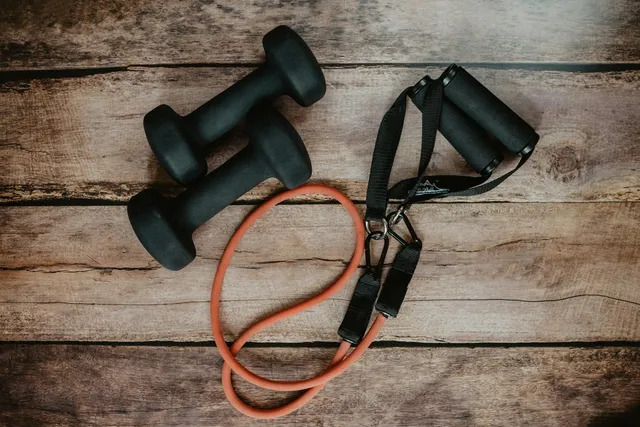 A pair of dumbbells and a resistance band lying on a wooden surface, none of it connected to anything