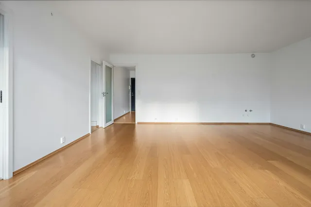 An empty apartment room with a bare wooden floor and white walls, before anything is moved in