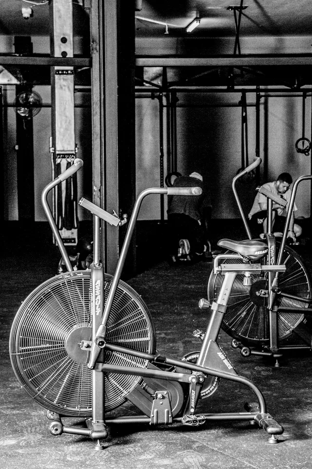 Two air bikes standing side by side in an empty gym, photographed in black and white