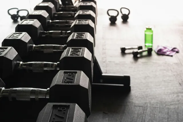 A rack of fixed hex dumbbells in ascending order with small weights and a bottle on the floor beside it