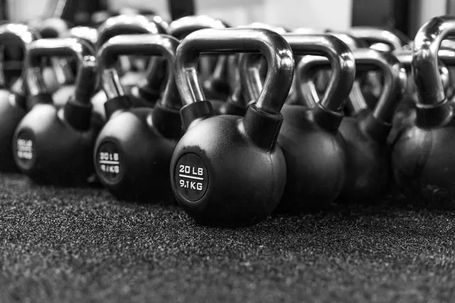 A row of cast iron kettlebells lined up on a gym floor, the nearest marked 20 lb