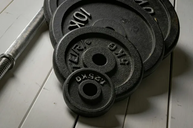 A stack of cast iron weight plates beside a threaded dumbbell handle on a pale floor