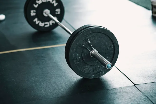 A loaded barbell resting on a hard gym floor, seen close to ground level