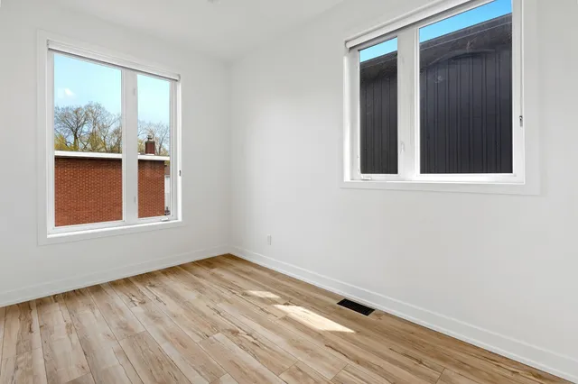 A bare room with pale wood flooring and windows on two walls, no furniture in it