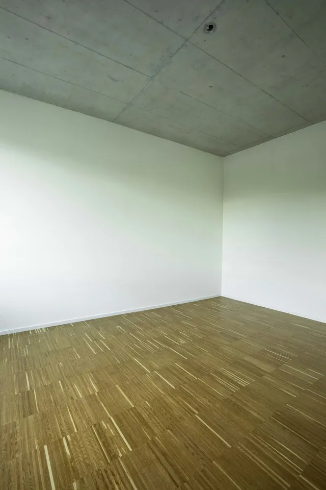 A bare wooden floor meeting two plain walls in an empty corner of a room