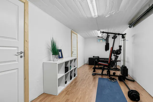 A narrow room under a sloped ceiling with a bench, a mat and a small stack of weights against the wall