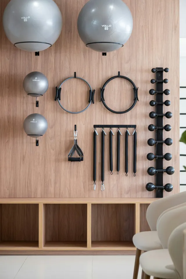 Kettlebells, dumbbells and small training tools mounted on a wooden wall panel above a low cabinet in a living room