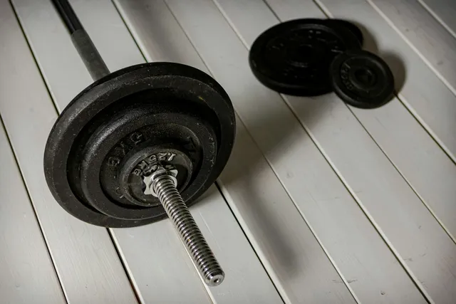 A threaded dumbbell handle loaded with plates and a screw collar, on a white floor