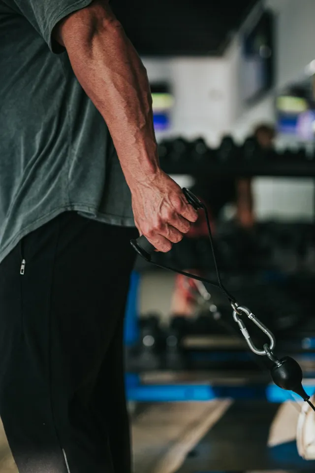 A man in a t-shirt and tracksuit trousers gripping a handle with the cord under tension